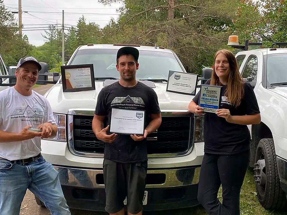 Three members of the Stokes Roofing team holding award certificates in front of the company's white pickup trucks