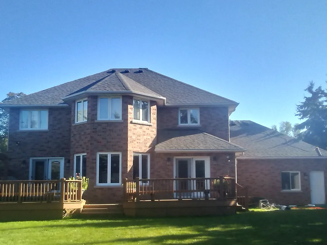 Brick two-storey home with a new grey roof, seen from the back yard