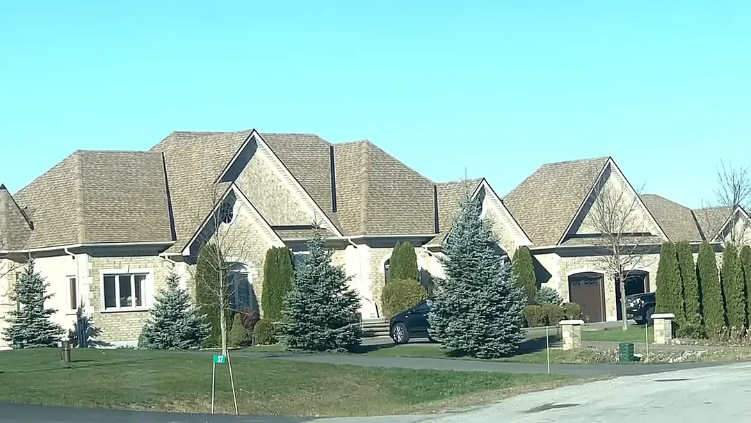 Large stone home with a finished light brown shingle roof and evergreen landscaping