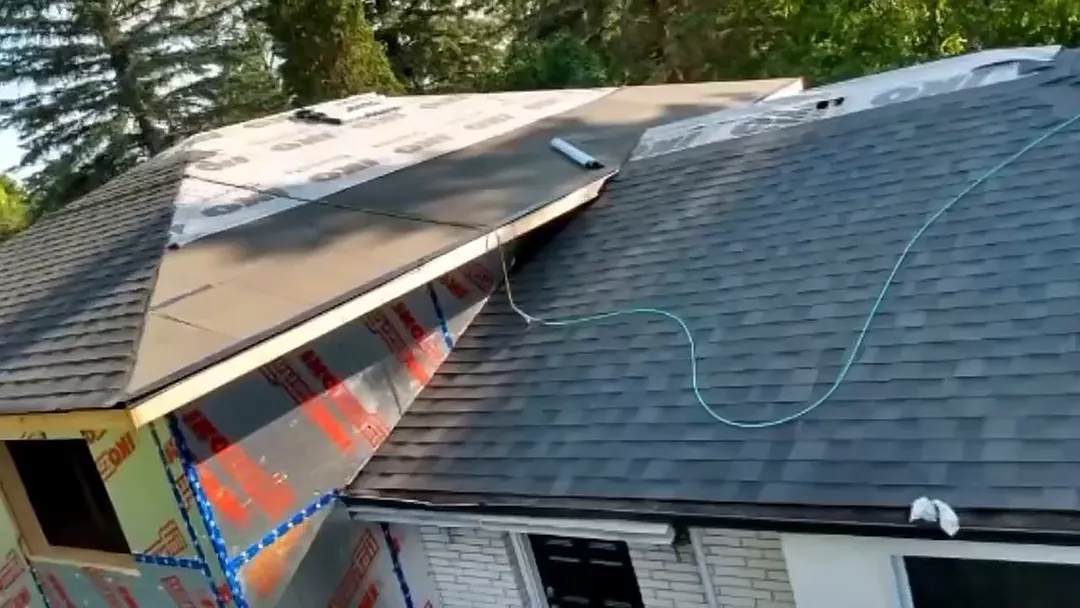 Roof mid-job: one side covered in new dark shingles, the other prepped for shingles, with the walls wrapped